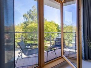 A balcony with a glass door, a table with chairs, and a view of a green park with trees and a road. - Urlaub auf Usedom - Ferienwohnung Tower 13 by Interhome (Swinoujscie)