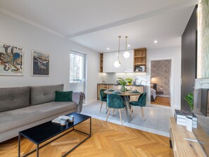A modern living room with a sofa, coffee table, and dining area with chairs. There is a kitchen in the background with cabinets and a dining table. - am Meer, Urlaub auf der Insel Usedom, Apartment Matejki 16 by Interhome (Swinoujscie)