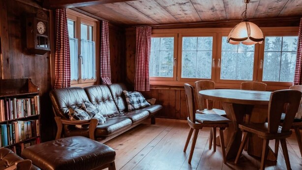 Interior acogedor de una cabaña con sofá de cuero, mesa de comedor de madera y estantería.