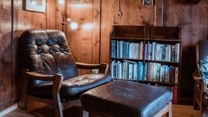 Una habitación acogedora con paredes de madera, un sillón de cuero, un banco de madera, una estantería y un reloj de pared.