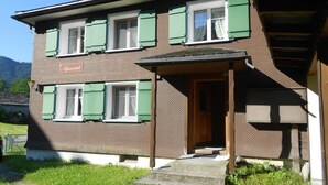 Un edificio de dos pisos con contraventanas verdes, una puerta de madera y un porche pequeño.
