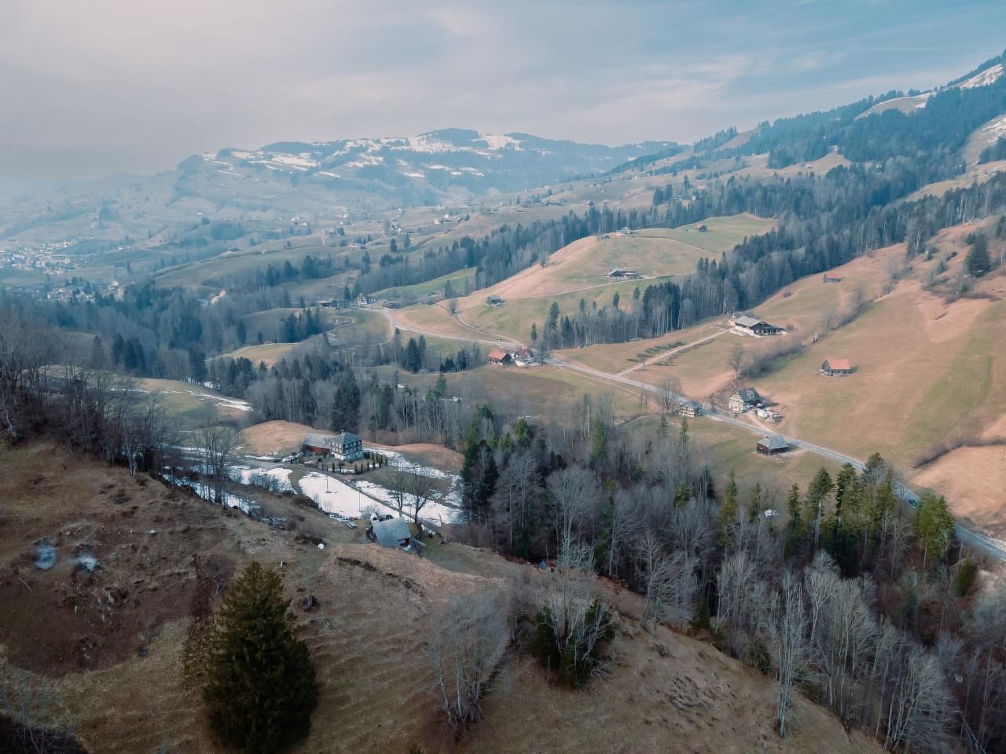 Vista panorâmica de uma paisagem montanhosa com casas dispersas e um rio.