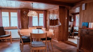 Un interior de madera con una mesa redonda rodeada de sillas, una zona de cocina con armarios de madera, y un rincón de descanso acogedor con un sofá y un sillón.