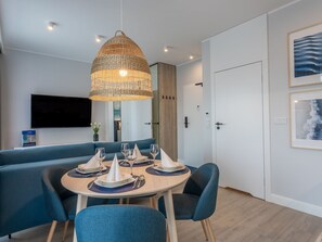 Ein moderner Essbereich mit einem runden Tisch, gedeckt für vier Personen, einem blauen Sofa und einer großen, gewebten Pendelleuchte.