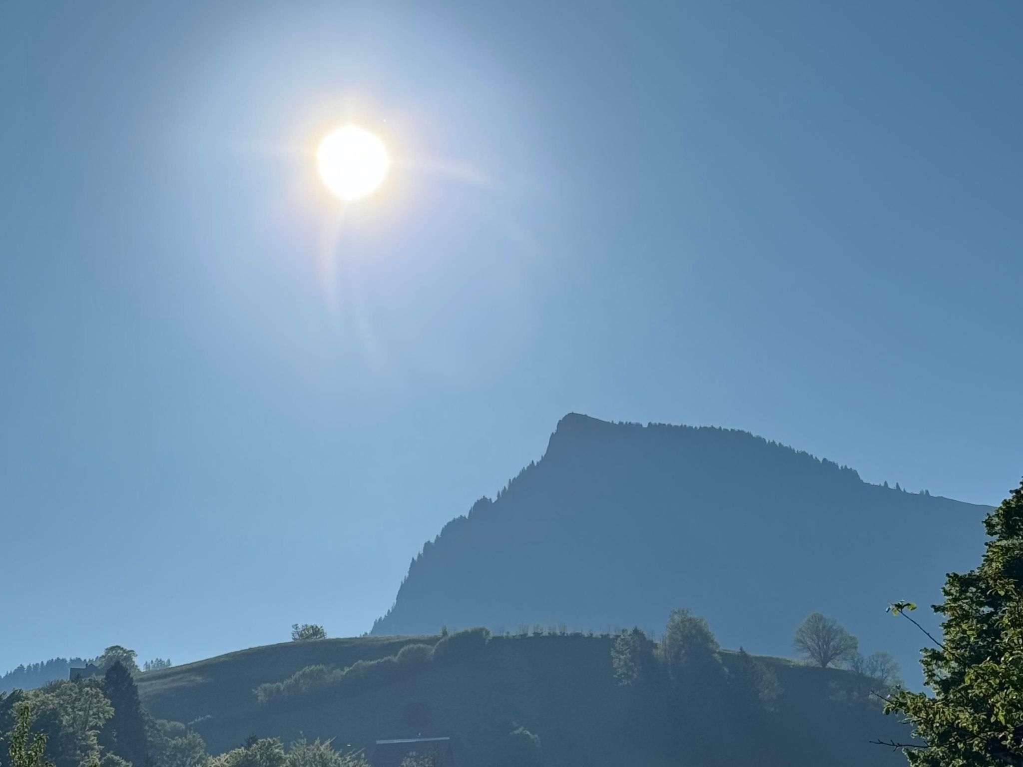 A mountain with a clear sky and the sun shining.