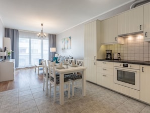 A modern kitchen with white cabinetry, a dining area with a white table and chairs, and a large window with curtains. - Zuza mit schönem Sonnenbalkon by Interhome (Swinoujscie)