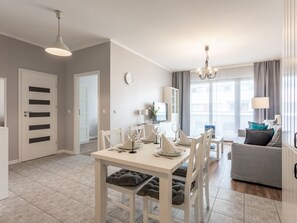 A modern living room with a dining area, a grey sofa, a chandelier, and a large window with curtains. - Zuza mit schönem Sonnenbalkon by Interhome (Swinoujscie)