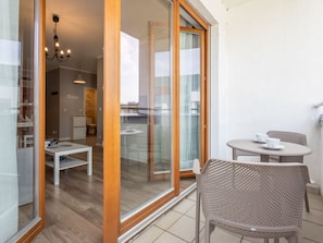 A modern apartment with a glass door leading to a balcony, a dining area with a table and chairs, and a living room with a sofa and a chandelier. - Zuza mit schönem Sonnenbalkon by Interhome (Swinoujscie)