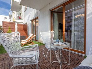 Eine Terrasse mit zwei weißen Korbstühlen, einem kleinen runden Tisch mit einem Buch und einer Tasse, sowie einem Holzboden.