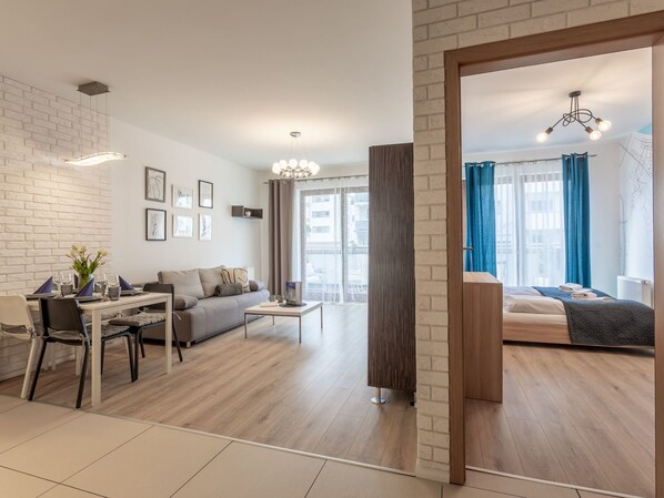 Ein modernes Wohnzimmer mit Sofa, Couchtisch und Essbereich. Ein großes Fenster mit Vorhängen, eine Pendelleuchte und Blick auf die Stadt.