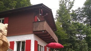 Un bâtiment à deux étages avec une façade rouge et blanche, un balcon et un parasol rouge.