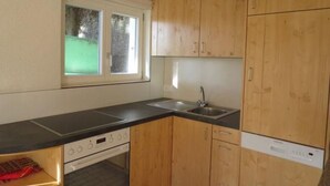 Une cuisine compacte avec des meubles en bois, un plan de travail noir, un four encastré et une fenêtre donnant sur un paysage verdoyant.