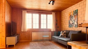 Una habitación acogedora de estilo cabaña con paredes de madera, un sofá, un televisor y un ventanal con cortinas.