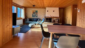Interior acogedor de una cabaña con techo de madera, chimenea, sofá y mesa de comedor.