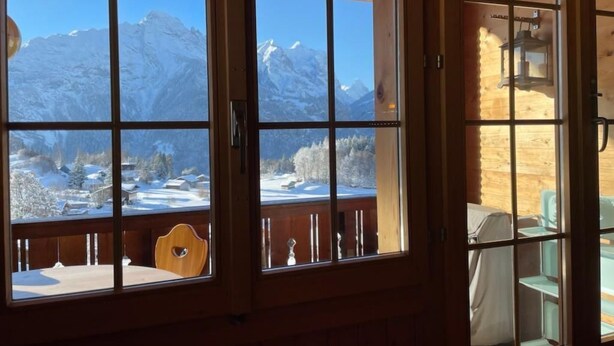 Una cabaña de madera con ventanas amplias que ofrecen vistas a montañas nevadas.