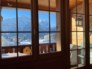 Une cabane en bois dotée de grandes fenêtres qui offrent une vue sur des montagnes enneigées.