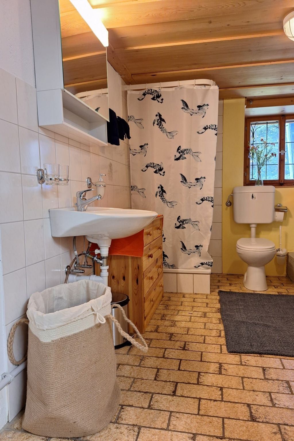 Ein Badezimmer mit Waschtisch aus Holz, Spüle, Toilette und einer Duschvorhang mit Vogelmotiv.