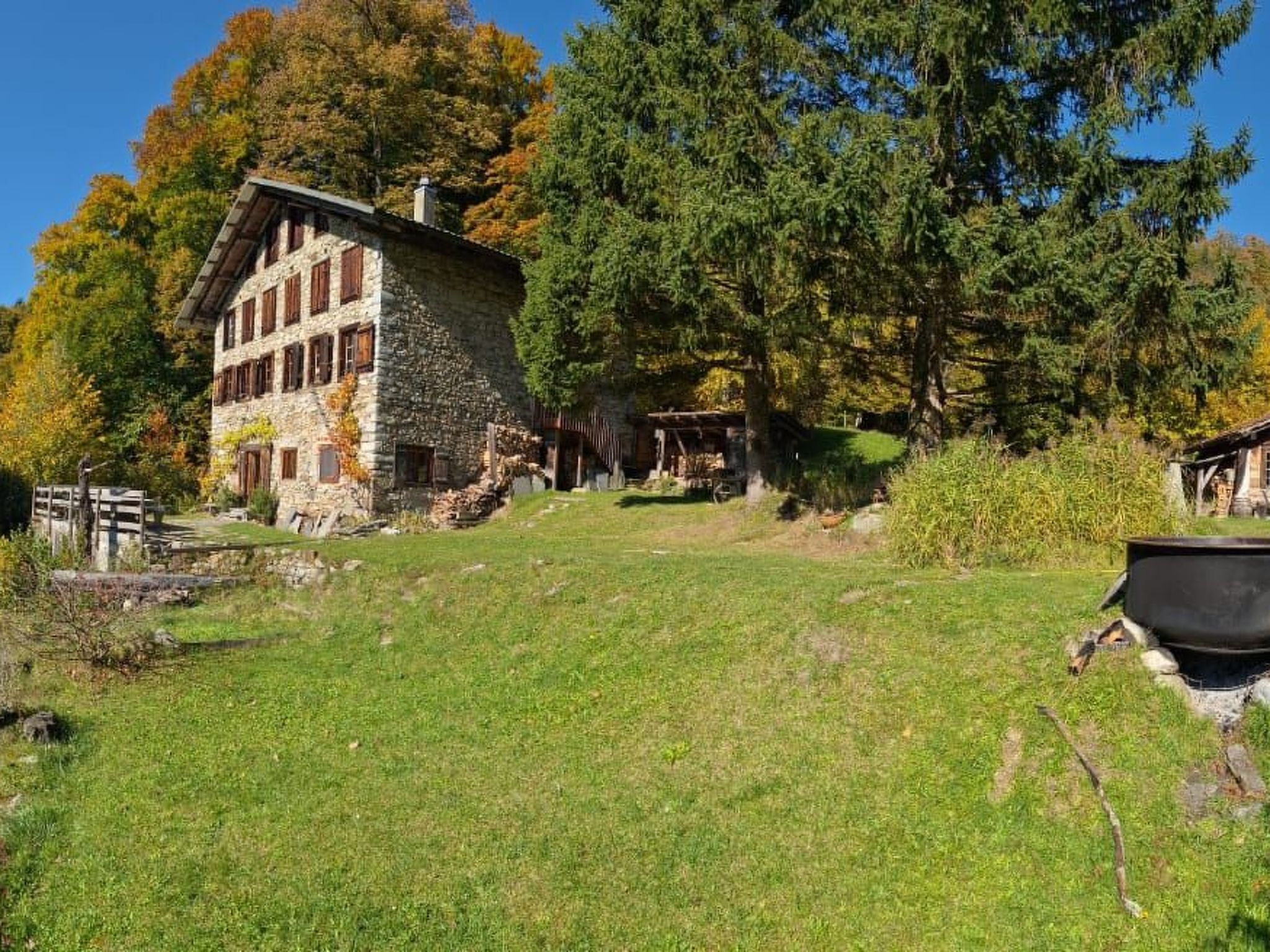 Ein Steinhaus mit geneigtem Dach und zahlreichen Fenstern, umgeben von einer Rasenfläche und Bäumen.