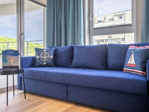 A blue sofa with nautical-themed pillows, a framed picture of a windmill, and a small table with a similar picture. - Urlaub auf Usedom, Apartment Sun Towers A49 by Interhome (Swinoujscie)