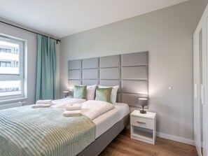 A modern bedroom with a large bed, a headboard, a bedside table, and a window with curtains. - Urlaub auf Usedom, Apartment Sun Towers A49 by Interhome (Swinoujscie)