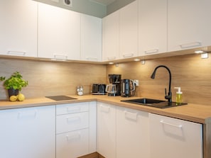 A modern kitchen with white cabinets, a wooden countertop, a black faucet, a Bosch coffee maker, and a potted lemon plant. - Urlaub auf Usedom, Apartment Sun Towers A49 by Interhome (Swinoujscie)
