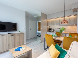 A modern living room with a flat-screen TV, wooden cabinets, a dining area with yellow chairs, and a kitchen with wooden cabinets and pendant lighting. - Ferienappartement del Sol auf Usedom by Interhome (Swinoujscie)