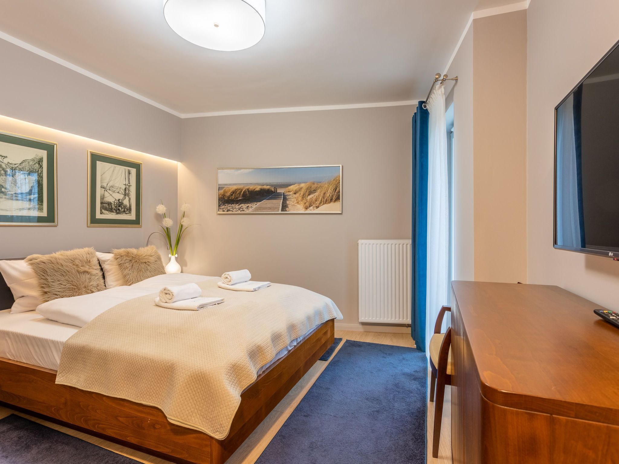 A bedroom with a wooden bed, a desk, a television, and artwork on the walls.