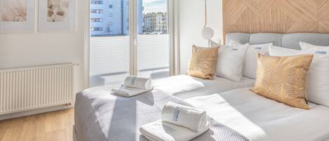 A modern hotel room with a large bed, a view of the city through floor-to-ceiling windows, and a wooden accent wall.