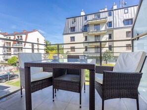 En balkong med möbler i rotting och ett bord i glas, med utsikt över ett bostadsområde med flerfamiljshus.