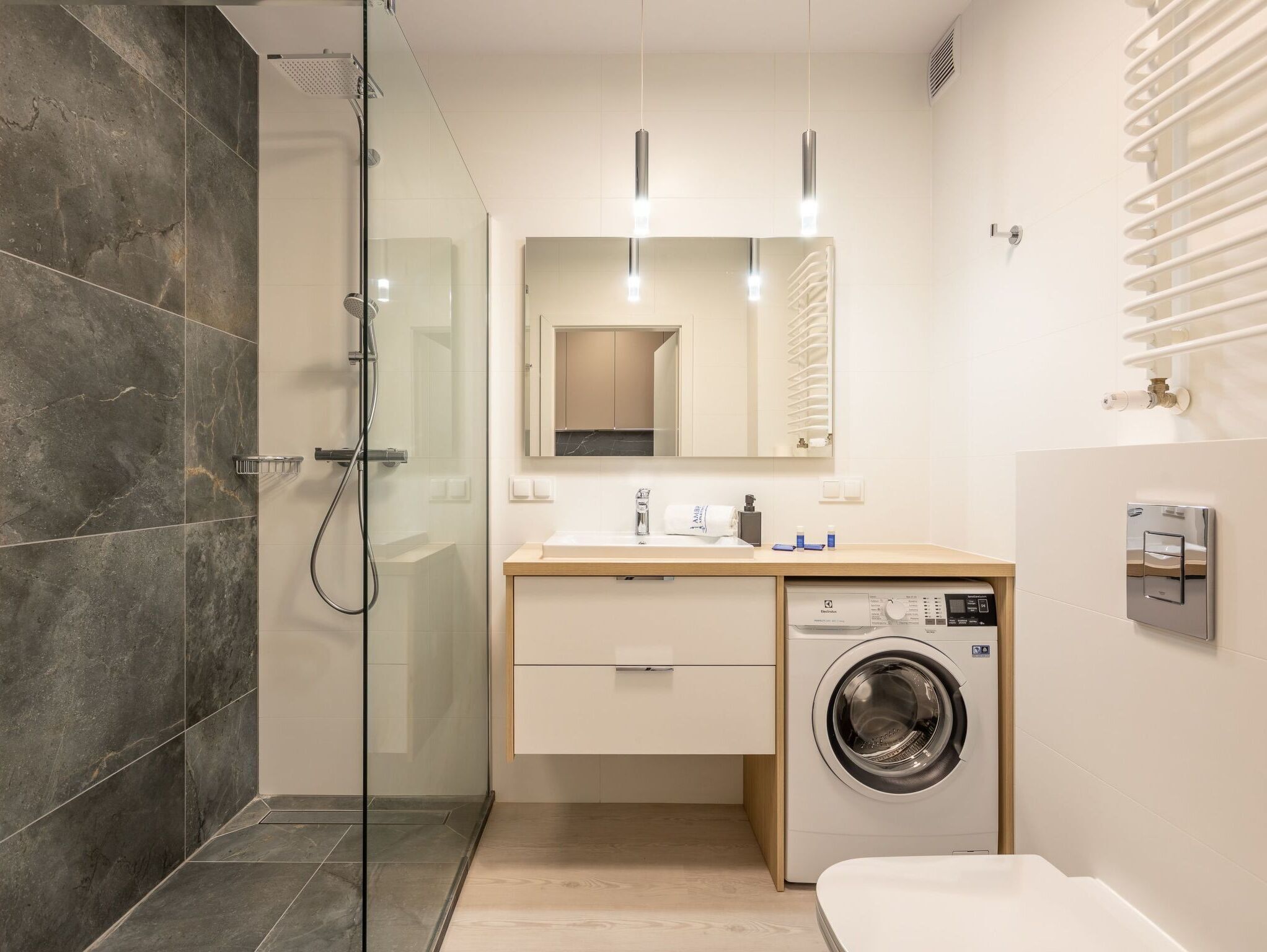 A modern bathroom with a glass-enclosed shower, a built-in washing machine, and a large mirror above the sink.