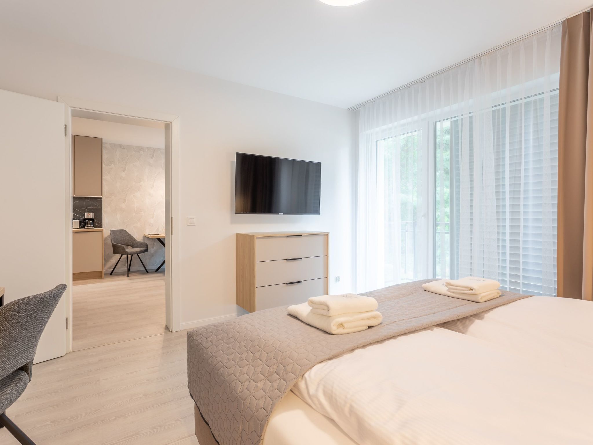 Une chambre d’hôtel moderne équipée d’un lit, d’une télévision, d’un bureau avec une chaise et offrant une vue sur l’extérieur grâce à de grandes fenêtres.