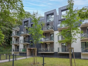 Ein modernes, mehrstöckiges Wohngebäude mit Balkonen, umgeben von Grünflächen und einem eingezäunten Garten.