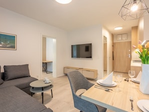 Ein modernes Wohnzimmer mit einer Couch, einem Esstisch für zwei Personen und einem an der Wand befestigten Fernseher.