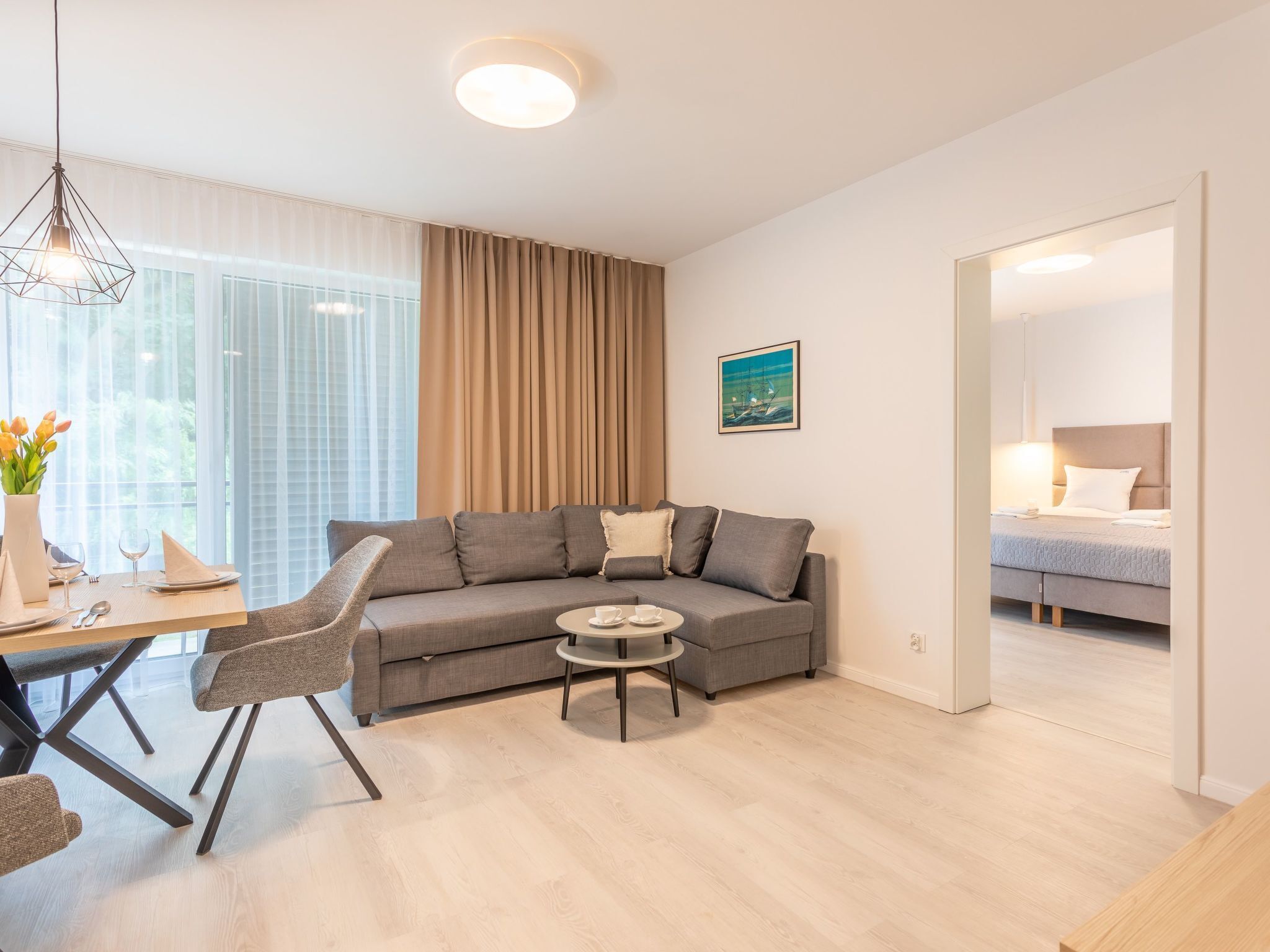En moderne stue med en grå sofa, et lille rundt sofabord og et spiseområde med et træbord og stole.