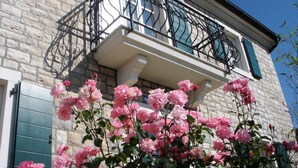 En byggnad i sten med en balkong som har smidesjärnsräcken och en blomlåda med rosa blommor.