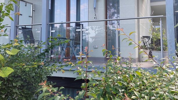 Un edificio moderno con ampie vetrate, un balcone con ringhiera in vetro e piante in vaso.