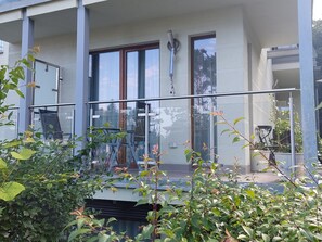 Ein modernes Gebäude mit großen Fenstern, einem Balkon mit Glasgeländer und Blumentöpfen.