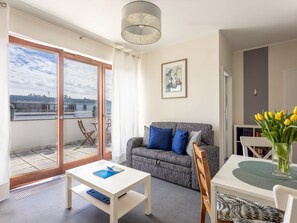 A modern living room with a grey sofa, a white coffee table, and a dining area with a white table and chairs. There is a balcony with a view of buildings and a door leading to another room. - Sky mit Balkon am Meer by Interhome (Swinoujscie)