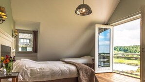A bedroom with a bed, a bedside table with a vase of flowers, a hanging light fixture, and a large window with a view of a green landscape. - Geräumiges Ferienhaus in Mechelen mit by Interhome (Mechelen)