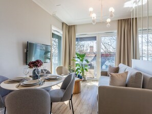 A modern living room with a round dining table, grey upholstered chairs, a beige sofa, and a large window offering a view of the city. - Jachtowa mit Terrasse auf Usedom by Interhome (Swinoujscie)