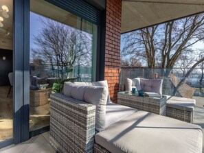 A modern outdoor seating area with wicker furniture and cushions, a glass table, and a view of trees and buildings. - Jachtowa mit Terrasse auf Usedom by Interhome (Swinoujscie)