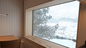 Una habitación con un ventanal grande que da a un paisaje nevado con árboles y montañas.