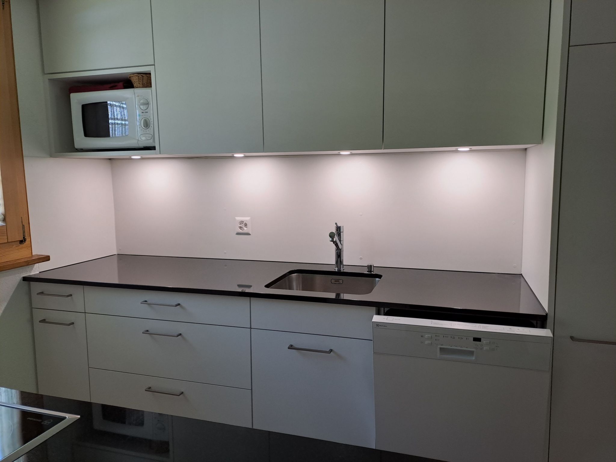 A modern kitchen with white cabinets, a black countertop, a built-in microwave, and a dishwasher.
