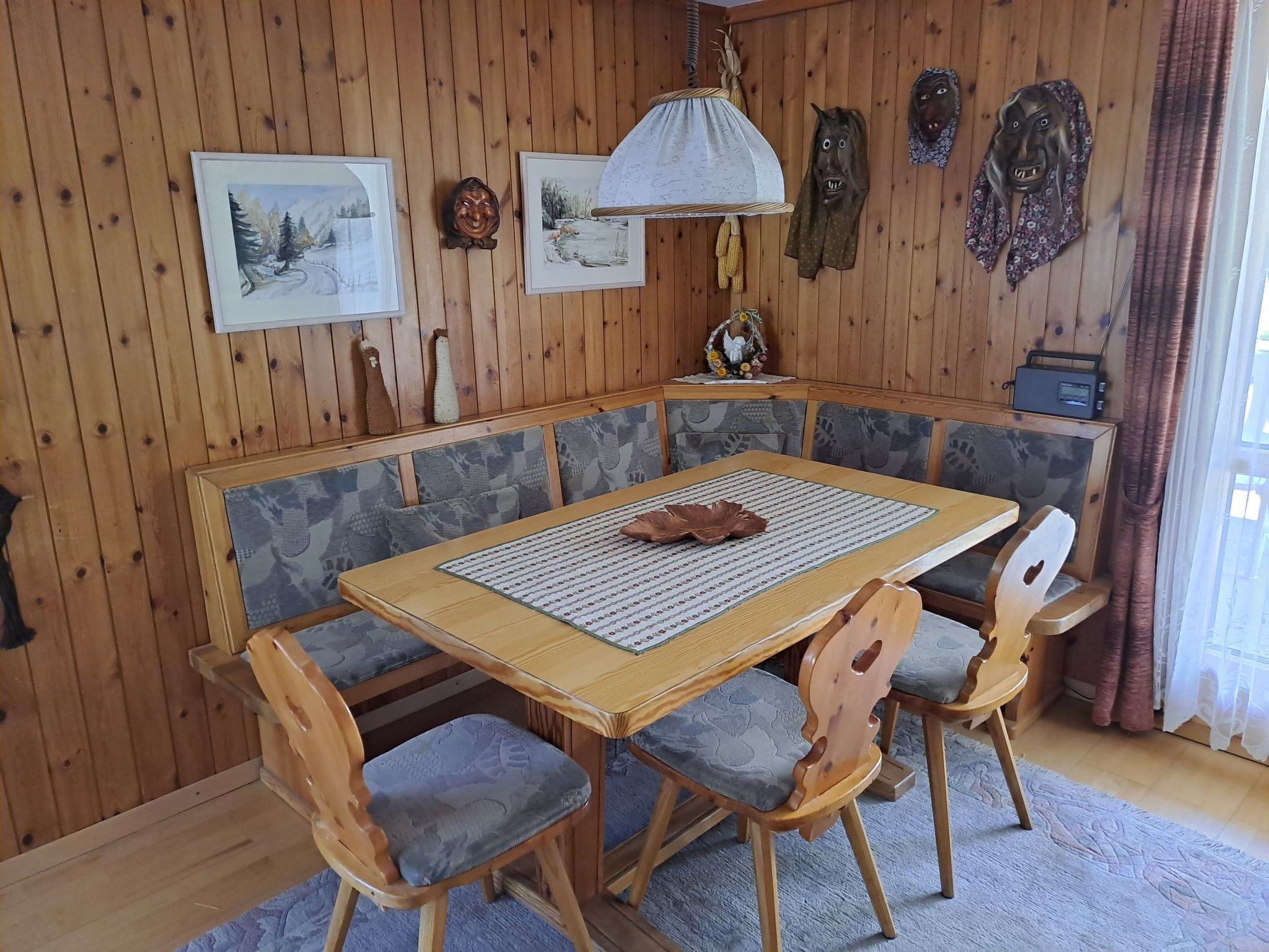 A wooden-paneled room with a dining table, cushioned chairs, and wall-mounted decorations.