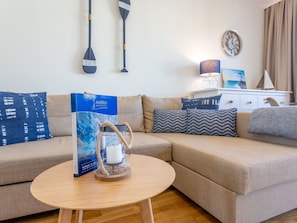 Ein Wohnzimmer mit einem beigefarbenen Sofa, einem runden Couchtisch und einer blauen Kiste auf dem Tisch.