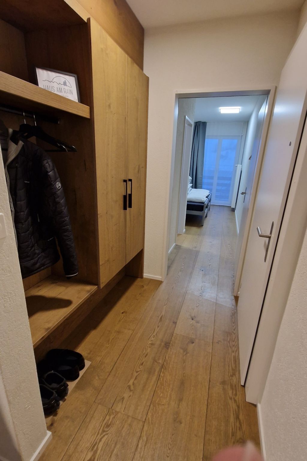 Een gang met houten vloer, een kapstok en een garderobe.