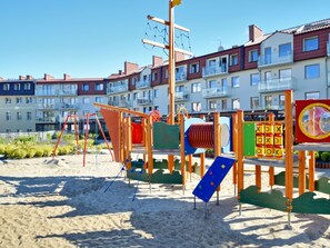 A playground with various play structures, including slides and climbing areas, situated on a sandy area with residential buildings in the background. - Verano direkt am Meer by Interhome (Swinoujscie)