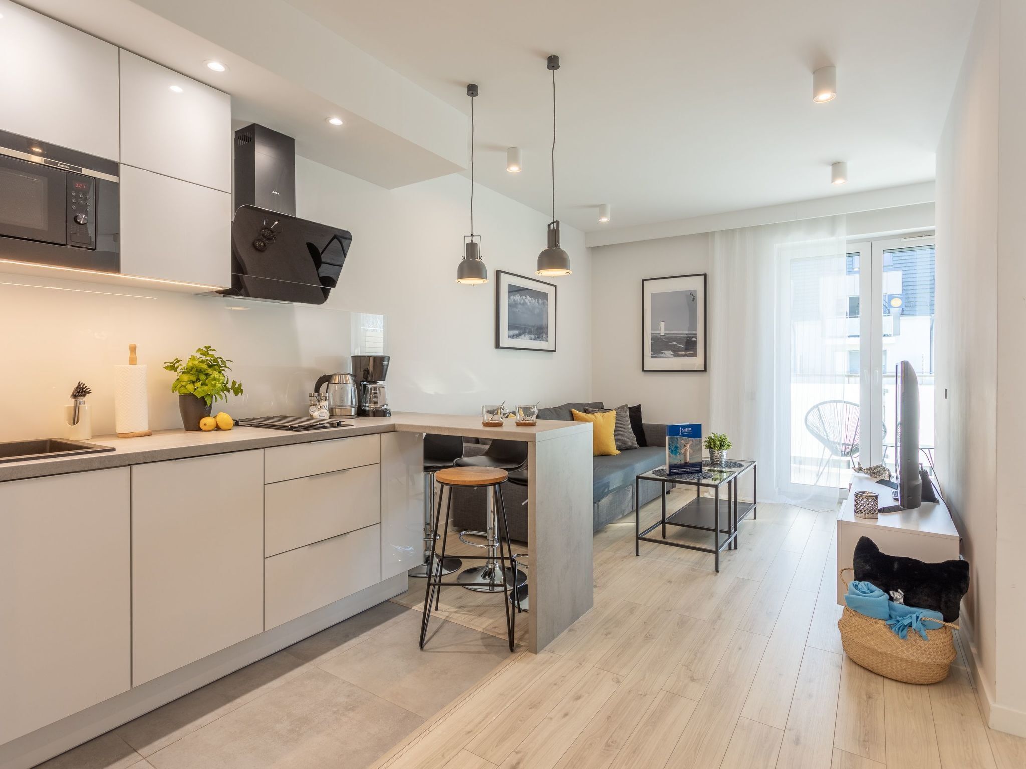 A modern kitchen with a built-in microwave, coffee maker, and bar stools. There is a dining area with a sofa and a coffee table.