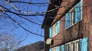 A two-story brick building with blue shutters, a visible satellite dish, and a pathway leading to a green lawn. - Neuer Sigerst by Interhome (Wildhaus)