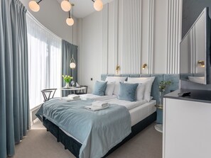 A modern hotel room with a large bed, a desk, and a chair. There is a window with curtains, a lamp, and a vase with flowers. - Helle Ferienwohnung mit Terrasse auf Usedom by Interhome (Swinoujscie)